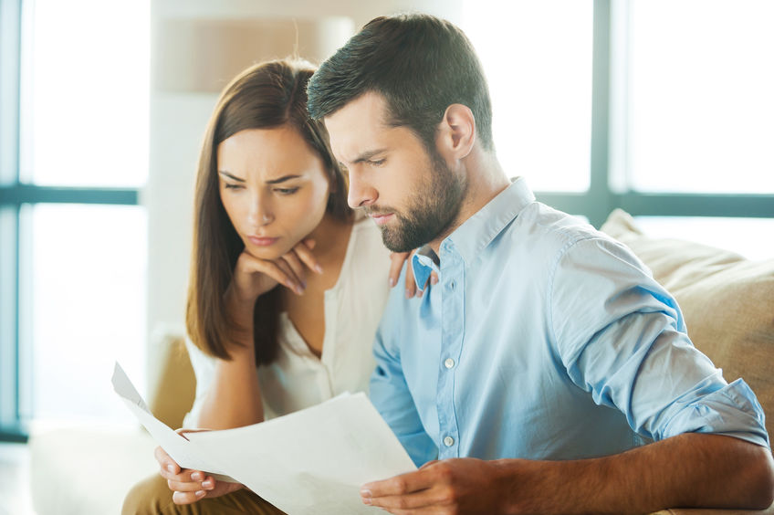 Examining documents together. Concentrated young man holding documents and looking at them while woman sitting close to him and holding hand on chin
