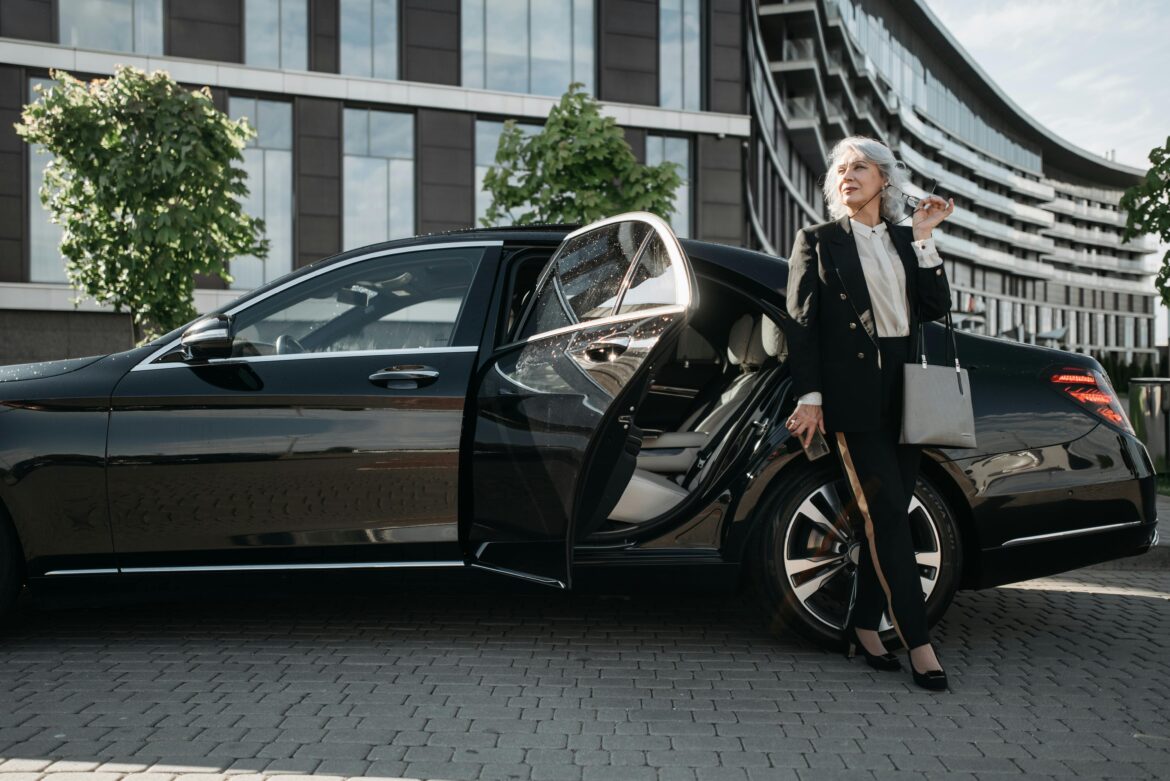 Elderly woman in black suit standing beside black car