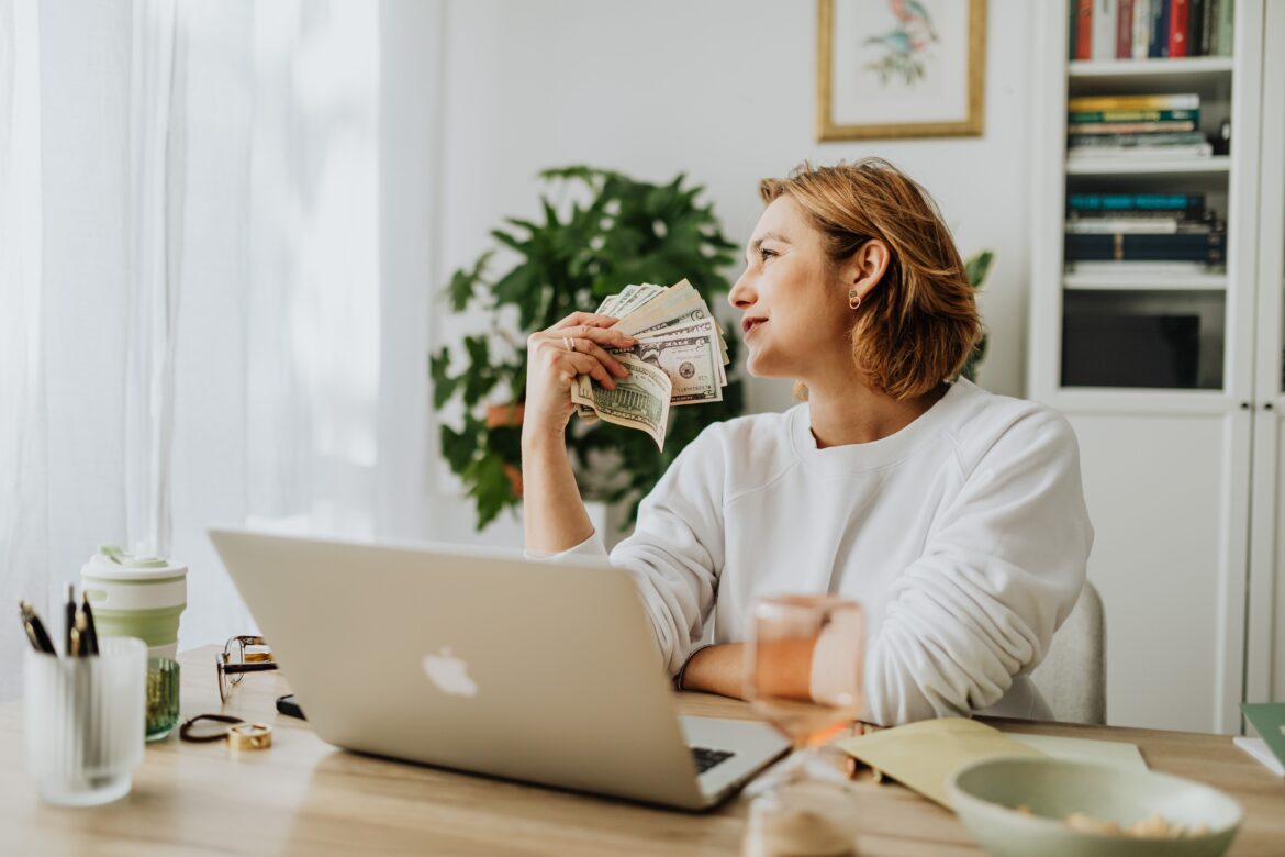 Woman sitting and holding money with laptop on desk