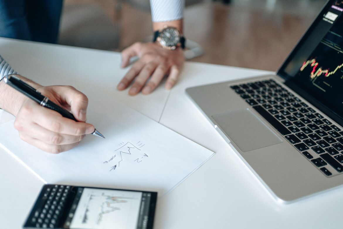 Person writing on a white paper beside the laptop and cellphone