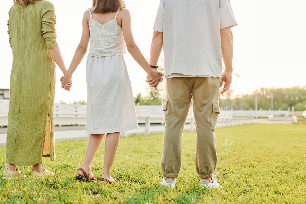 Three people standing hand in hand on grass field