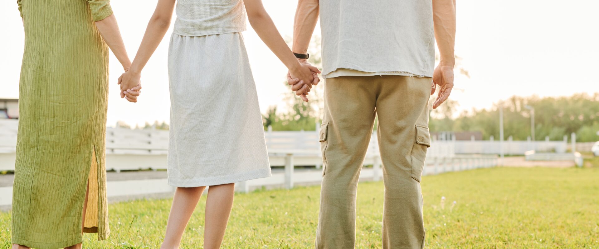 Three people standing hand in hand on grass field