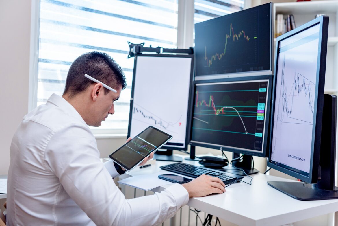 A man in white long sleeves using a computer with multiple displays