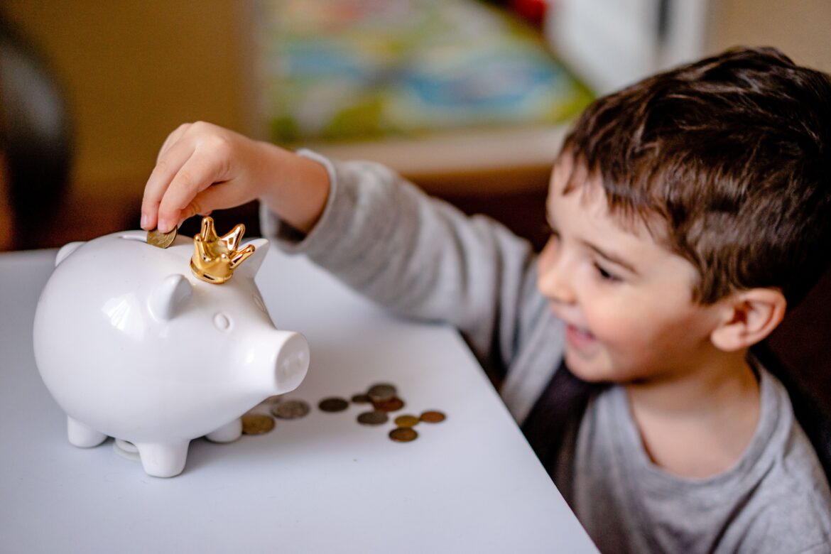 Boy in gray long sleeve shirt putting coins in a piggy bank