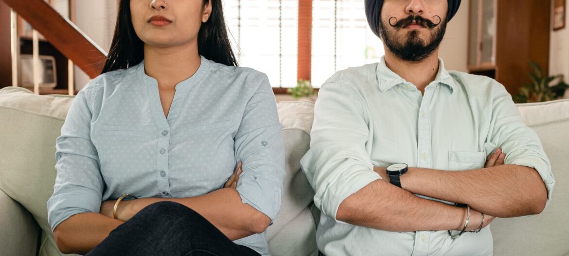 Crop serious ethnic couple with crossed arms on couch