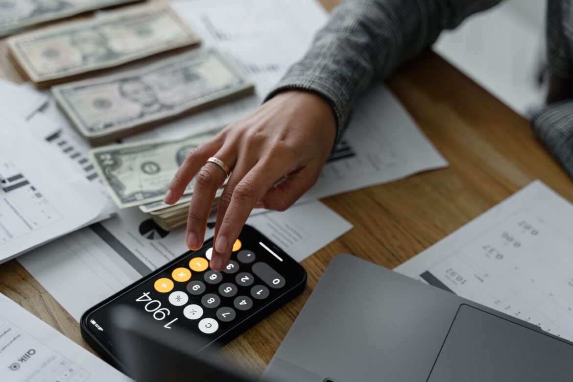 Hand of a person using a calculator near cash money on wooden table