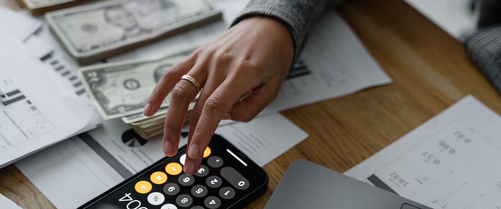 Hand of a person using a calculator near cash money on wooden table