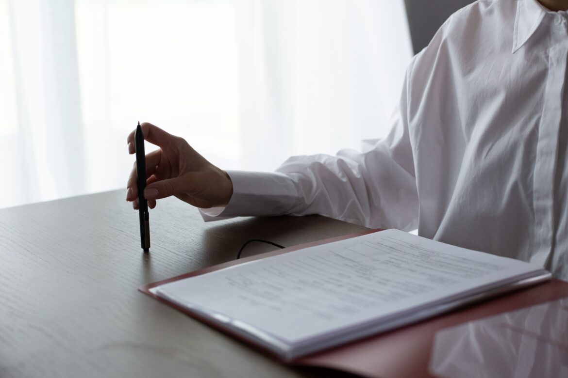 Unrecognizable hand of woman sitting at table and reviewing documents